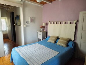 Un dormitorio con cama, mesita de noche, lámpara, reloj de pared y puerta.
