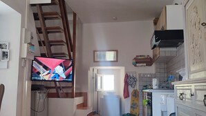 Amplia sala de estar con una escalera que lleva a un segundo piso, una cocina equipada con electrodomésticos modernos y un televisor mostrando una caricatura.