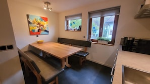 A compact kitchen with a wooden table, bench seating, a colorful abstract painting, and a window with a view of greenery. - Ski & Summer, luxury furnished vacation home close to lifts. Warm and cozy.   (Flachau)