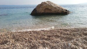 A pebble beach with a large rock formation in the water.