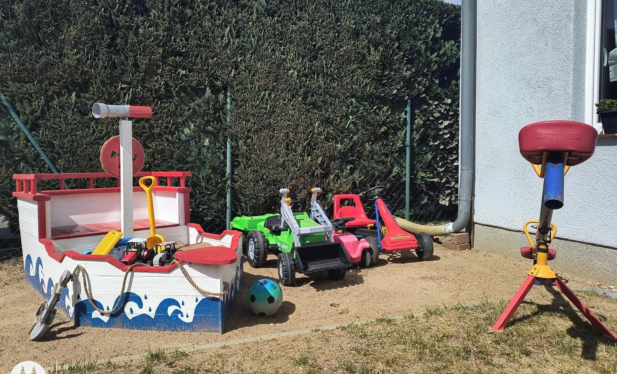 Un espace de jeux avec un bac à sable, des bateaux et des véhicules miniatures.