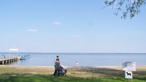 A beach with a grassy area, a pier, and a sign indicating no dogs allowed. - 4 * FH with garden, playground, sauna, fitness, 2 bedrooms, kitchen with dishwasher (Ludorf)