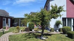 A residential building with a well-maintained garden, including a lawn, hedges, and a tree. - 4 * FH with garden, playground, sauna, fitness, 2 bedrooms, kitchen with dishwasher (Ludorf)
