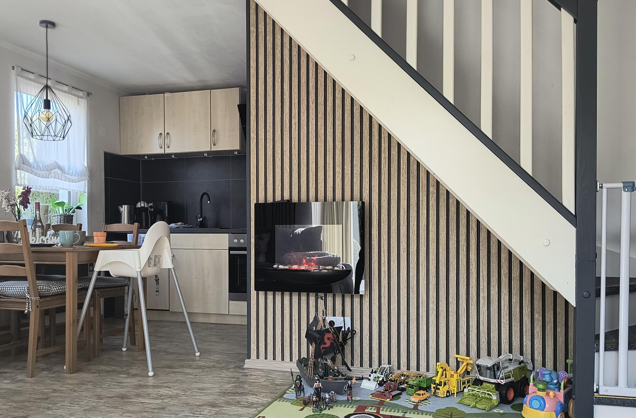 Une cuisine moderne avec des meubles en bois, un coin repas avec une table et des chaises, et un escalier avec un mur à rayures.