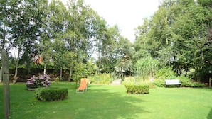 A well-maintained garden with a lawn, a wooden bench, and a metal chair. - Vacation apartment directly by the dike (Niedersachsen)