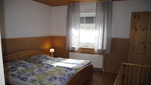 A bedroom with a wooden bed, a window with curtains, a radiator, and a wooden wardrobe. - Vacation apartment directly by the dike (Niedersachsen)