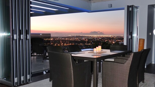 Un espace repas comprenant une table et des chaises, une cloison en verre et une vue sur le paysage urbain au crépuscule.