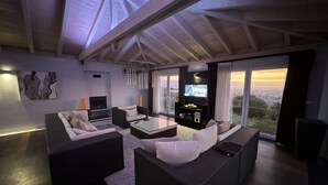 Un salon moderne avec un plafond haut, de grandes fenêtres et un téléviseur à écran plat.