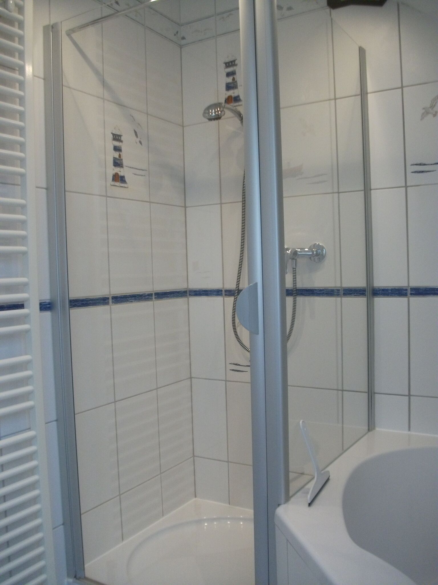 A modern bathroom with a glass-enclosed shower, white tiles, and a white bathtub.