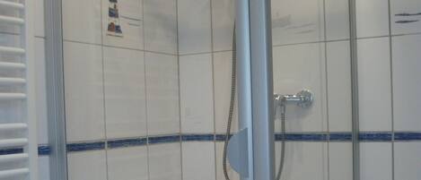A modern bathroom with a glass-enclosed shower, white tiles, and a white bathtub.