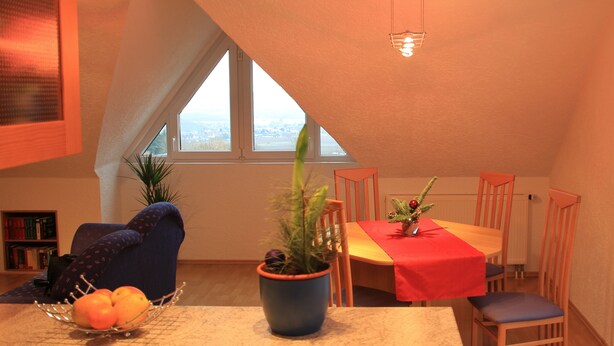 A dining area with a table, chairs, a potted plant, and a fruit bowl. - 3-star vacation apartment on the Rheinsteig with a magnificent view over the Rhine Valley (Rüdesheim am Rhein)