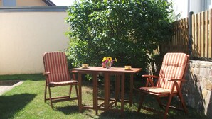 A wooden table with two striped chairs, a vase with flowers, and a stone wall in a backyard. - 3-star vacation apartment on the Rheinsteig with a magnificent view over the Rhine Valley (Rüdesheim am Rhein)