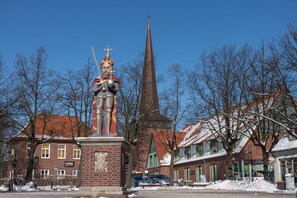 A statue of a knight in armor with a helmet and sword, standing on a pedestal in a town square.
