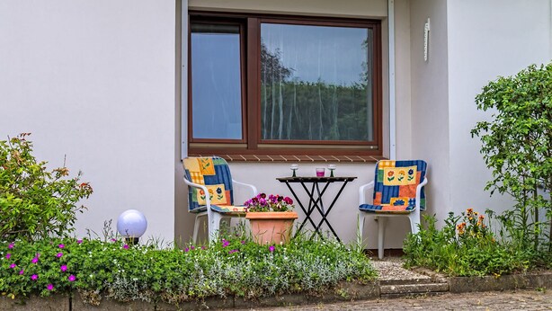 A small outdoor seating area with two chairs and a table, surrounded by a variety of plants and flowers. - Beautiful apartment in a central location in Wedel (Hamburg) (Wedel)