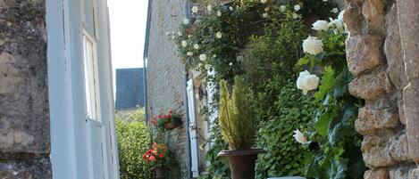 A stone wall with steps leading to a house. There are potted plants and flowers on the wall.