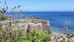 Une construction en pierre située sur la côte, avec des bateaux, une mer d’un bleu limpide et un paysage rocheux.