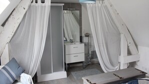 Un dormitorio con techo inclinado, un armario blanco, una mesita de noche y una lámpara colgante.