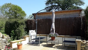 Una terraza de madera con una mesa, sillas, una planta en maceta y una pérgola con sombrilla.
