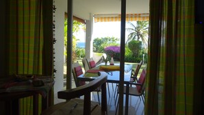 Una habitación con puerta de vidrio corredera que da a un espacio exterior con mesa y sillas, vistas al exterior y una pequeña mesa con una silla dentro de la habitación.