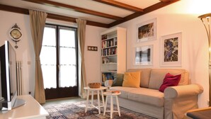 Een woonkamer met een bank, een kleine tafel, een boekenkast en een raam met gordijnen.