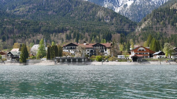 Uitzicht op een meer met traditionele chalets, een steiger en een achtergrond van besneeuwde bergen.