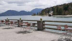 Een terras aan het meer met zitplaatsen buiten en uitzicht op bergen en een huis aan de overkant van het water.