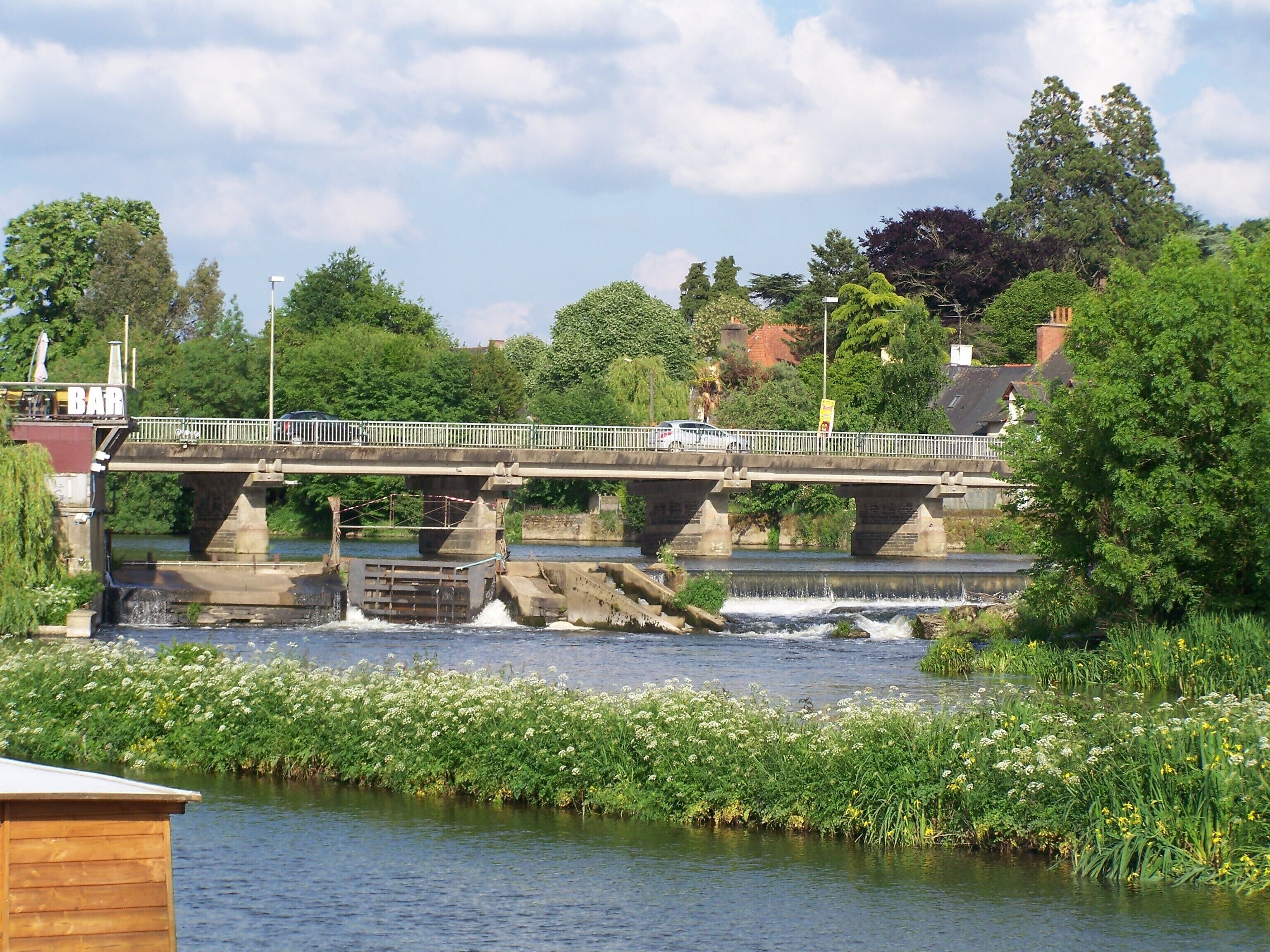 Un pont enjambant une rivière, avec un bar situé à gauche et un bâtiment à droite.