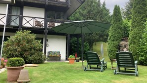 Un edificio de dos pisos con un balcón, un patio cubierto con sillas y un césped bien cuidado.
