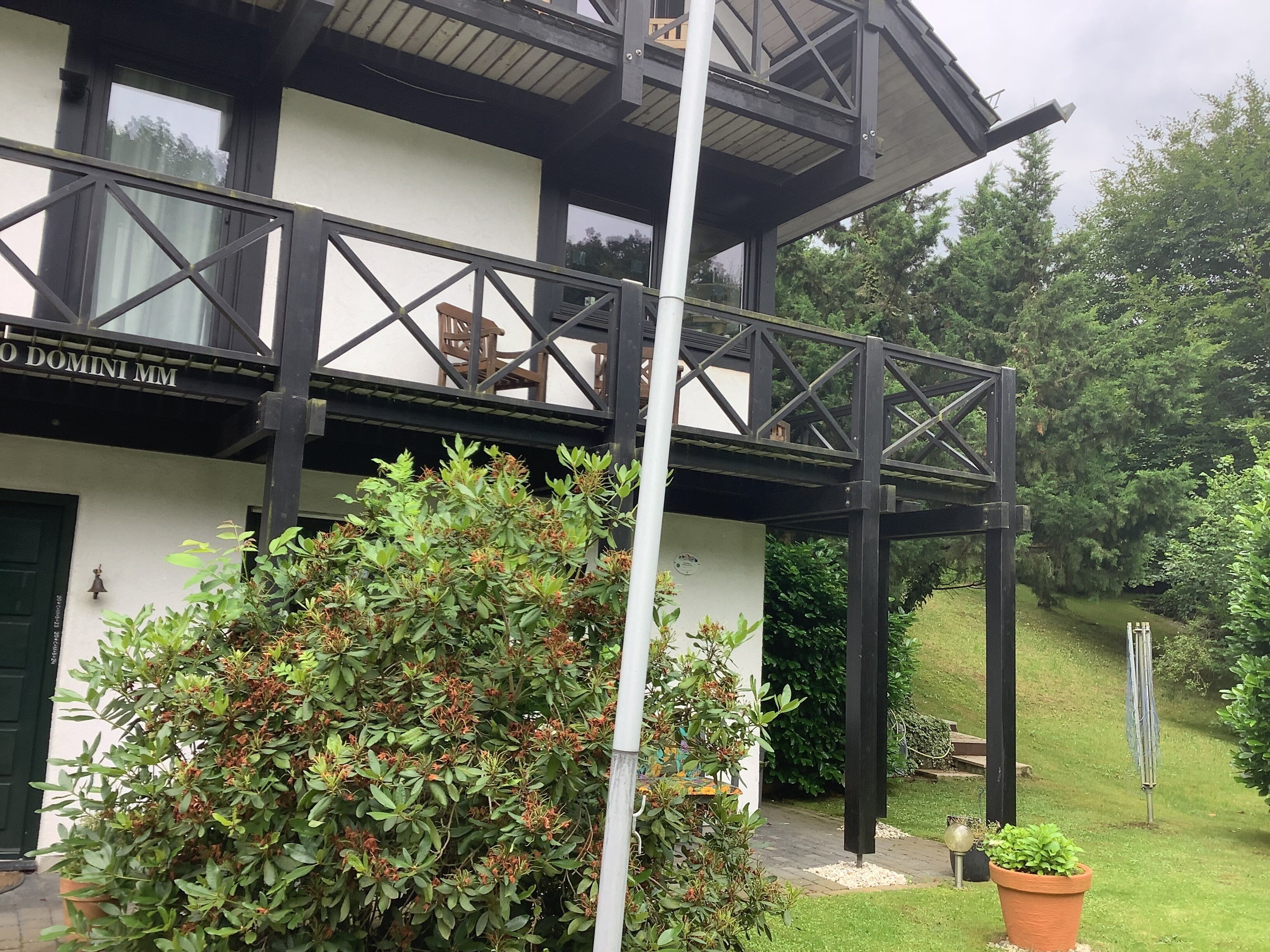 A two-story building with a balcony, a sign reading "DOMINI MM", and a well-maintained garden.