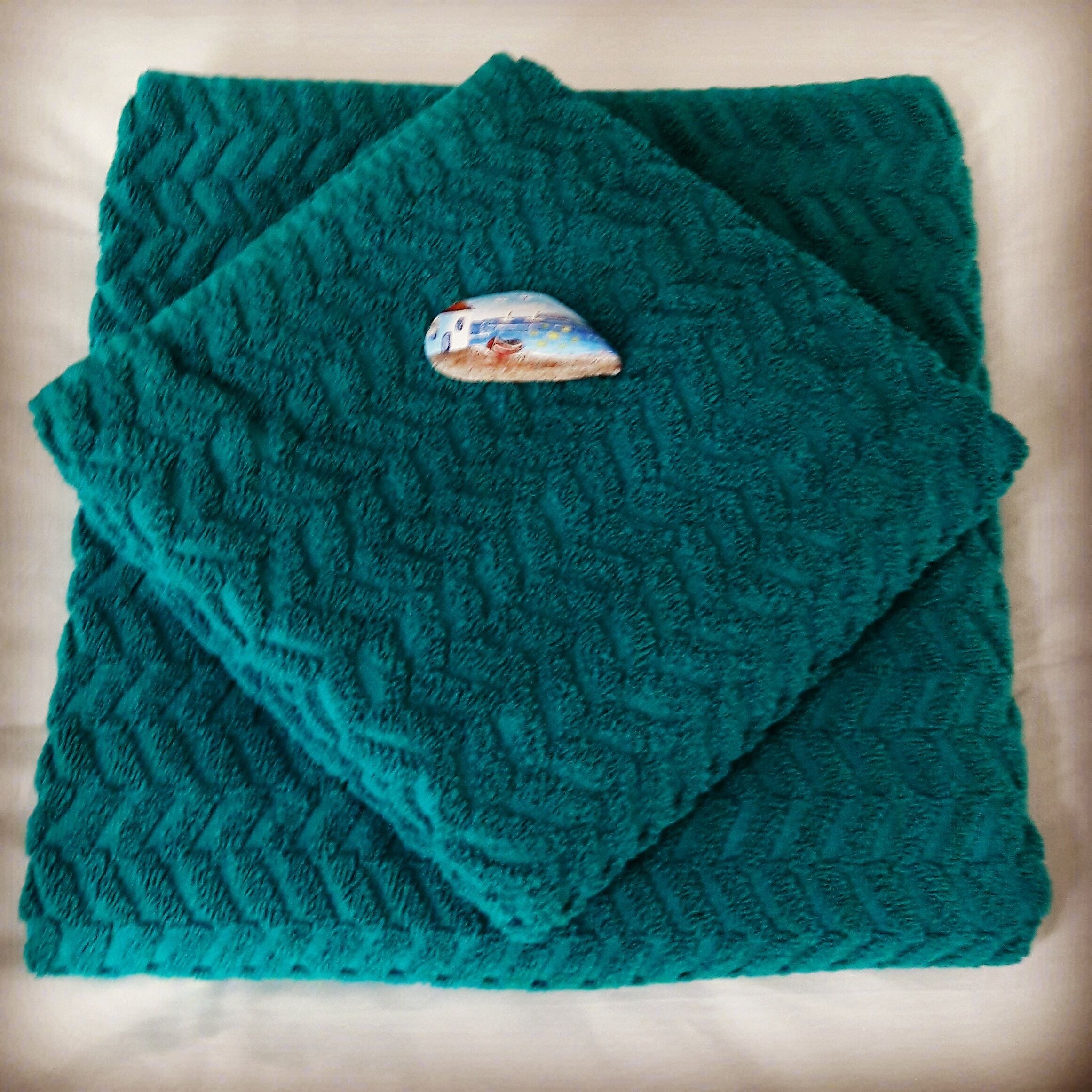 A teal textured blanket with a decorative patch on top.