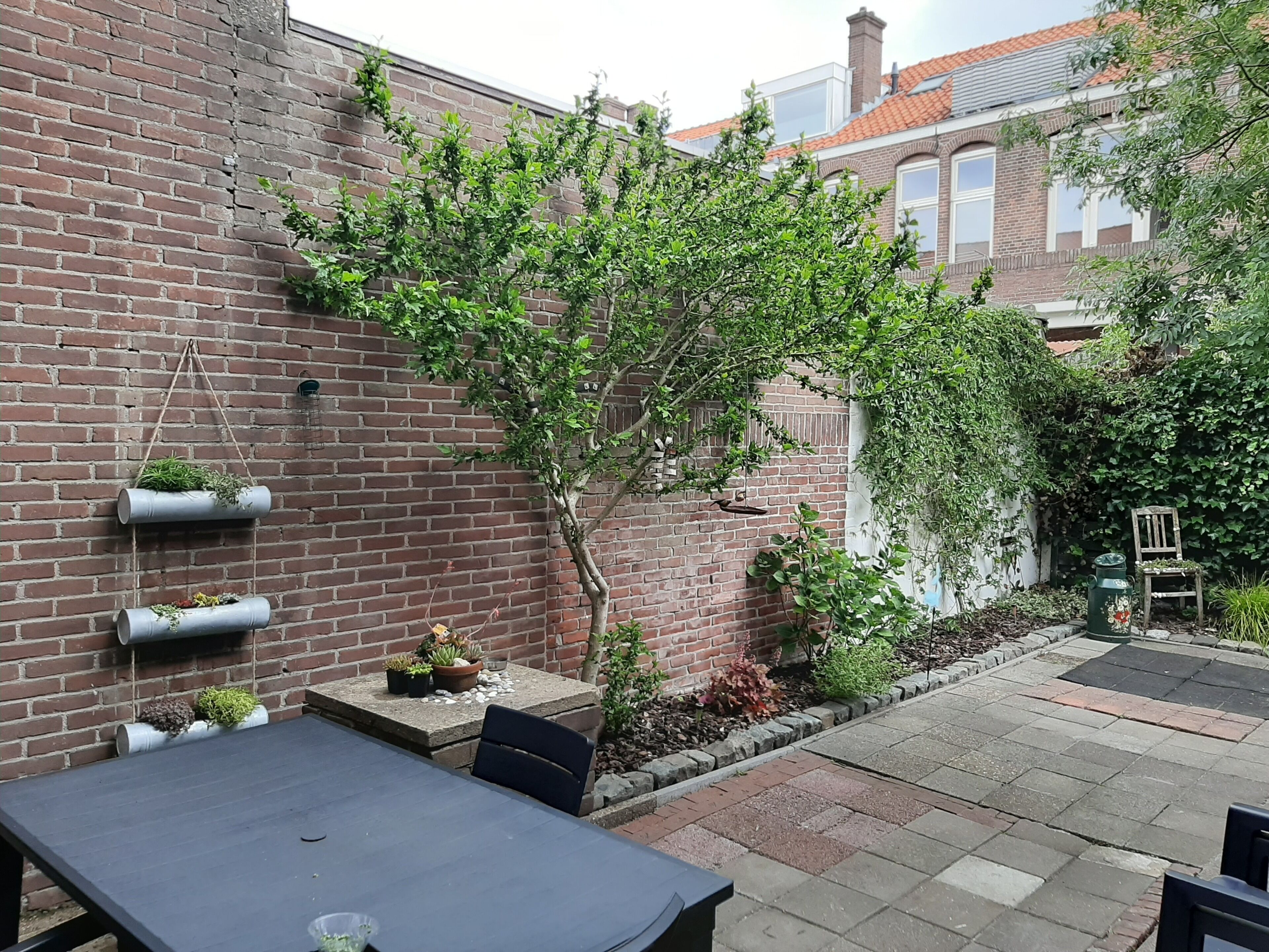 A brick wall with vertical garden planters, a small tree, and a patio area with a table and chairs.