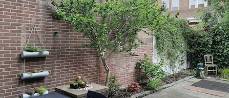 Un mur de briques agrémenté de jardinières verticales, un petit arbre et un espace patio avec une table et des chaises.