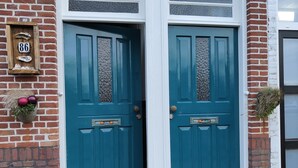 A double door with a white frame and a teal door, set in a brick wall with a small mailbox and a number plate. - Characteristic apartment, renovated, 500m from the sea, beach and town center (Vlissingen)