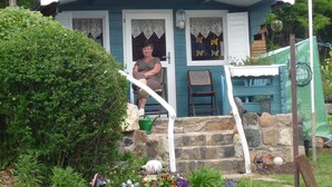 A small house with a porch, a chair, and a garden with flowers and a statue.