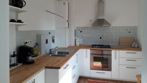 Una cuina moderna amb armaris blancs, taulell de fusta, forns de gas, forn, rentapelats i campana extractora.