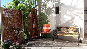 Zona de jardí amb una banca de fusta, una tanca de bambú i plantes amb flors.