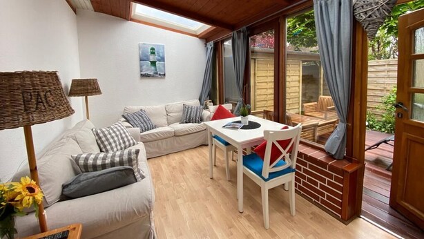 Ein gemütliches Wohnzimmer mit einer Couch, einem Esstisch und einem Fenster mit Blick auf einen Garten.
