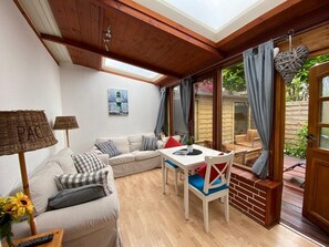 Un salon confortable avec un canapé, une table à manger et une fenêtre donnant sur un jardin.