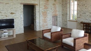 Un vaste salon doté d’un haut plafond, de poutres apparentes, d’une cheminée et d’un téléviseur posé sur un meuble en bois.