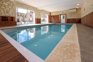 An indoor swimming pool with stone walls and wooden paneling, large windows, and a view of the outside.
