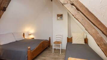 Une petite chambre mansardée, chaleureuse et accueillante, avec deux lits en bois, une chaise blanche et un petit tableau encadré accroché au mur.
