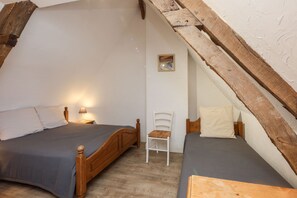 A small, cozy attic bedroom with two wooden beds, a white chair, and a small framed picture on the wall.