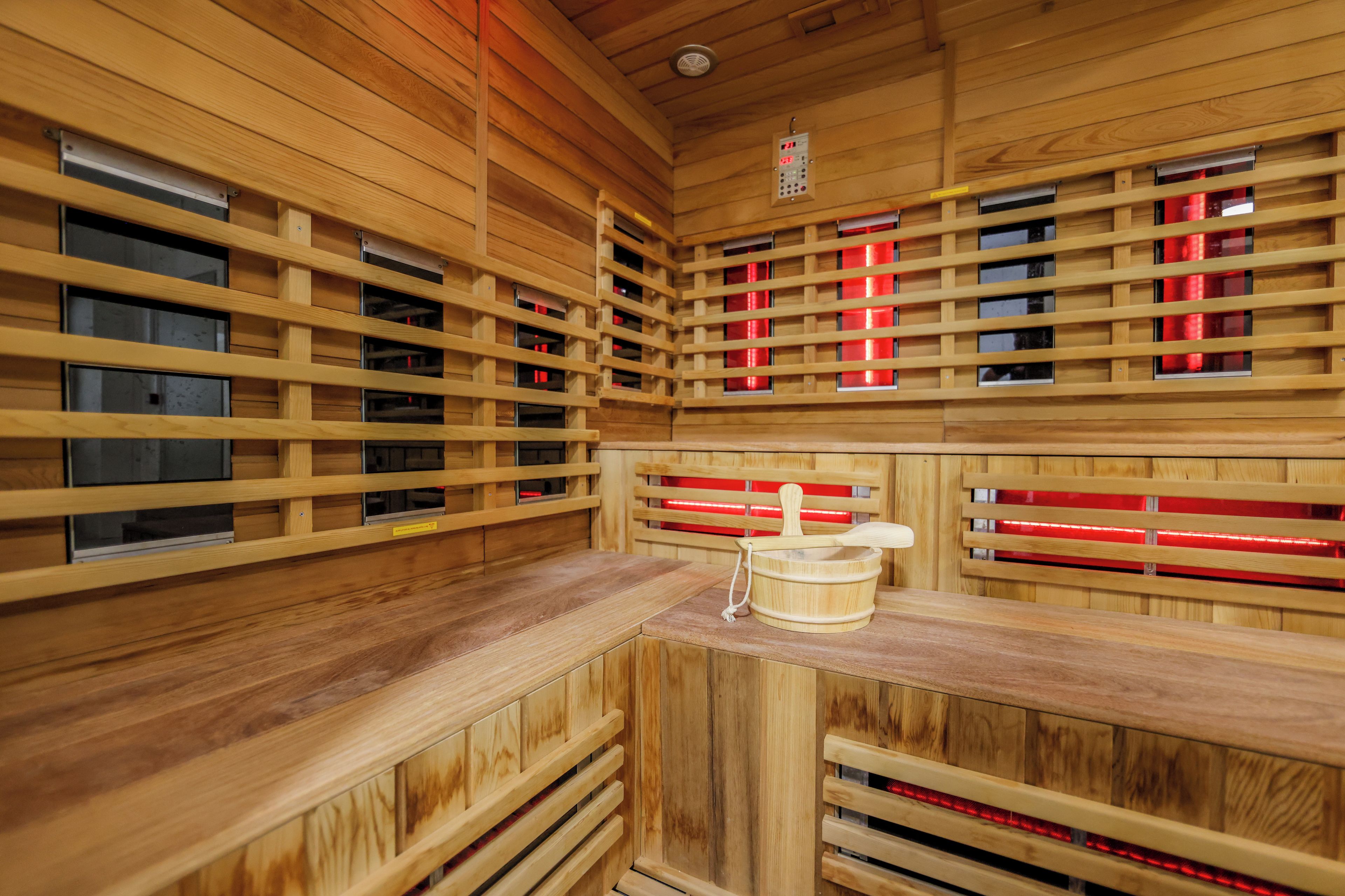 A sauna with wooden walls and benches, a control panel, and red lighting.