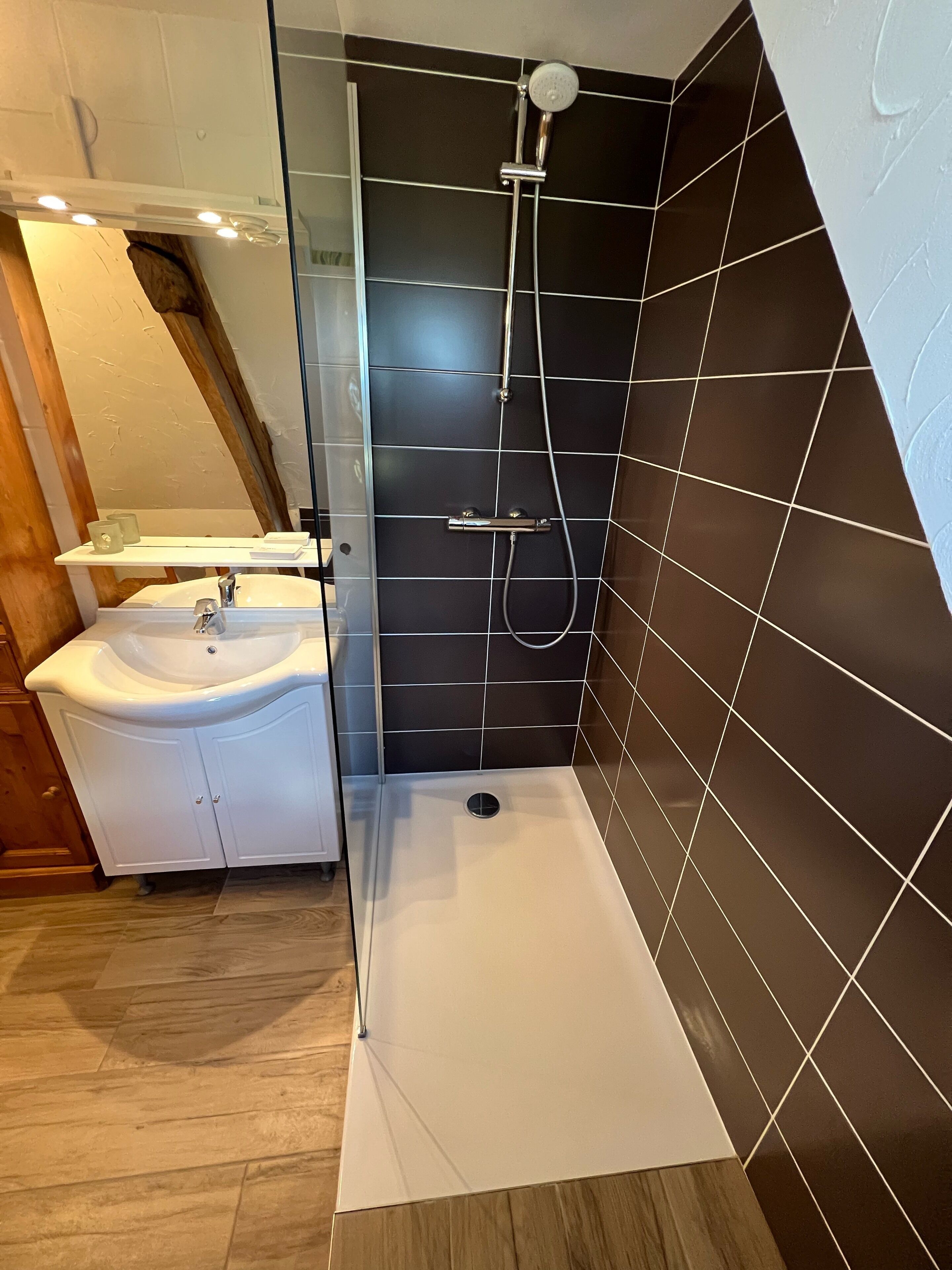 A modern bathroom with a glass-enclosed shower, a white sink, and a wooden vanity.
