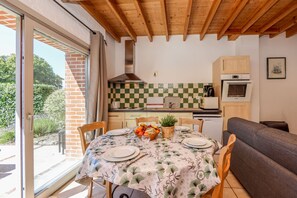 Una cocina con salpicadero a cuadros, armarios de madera, horno empotrado y una zona de comedor con una mesa dispuesta para dos.
