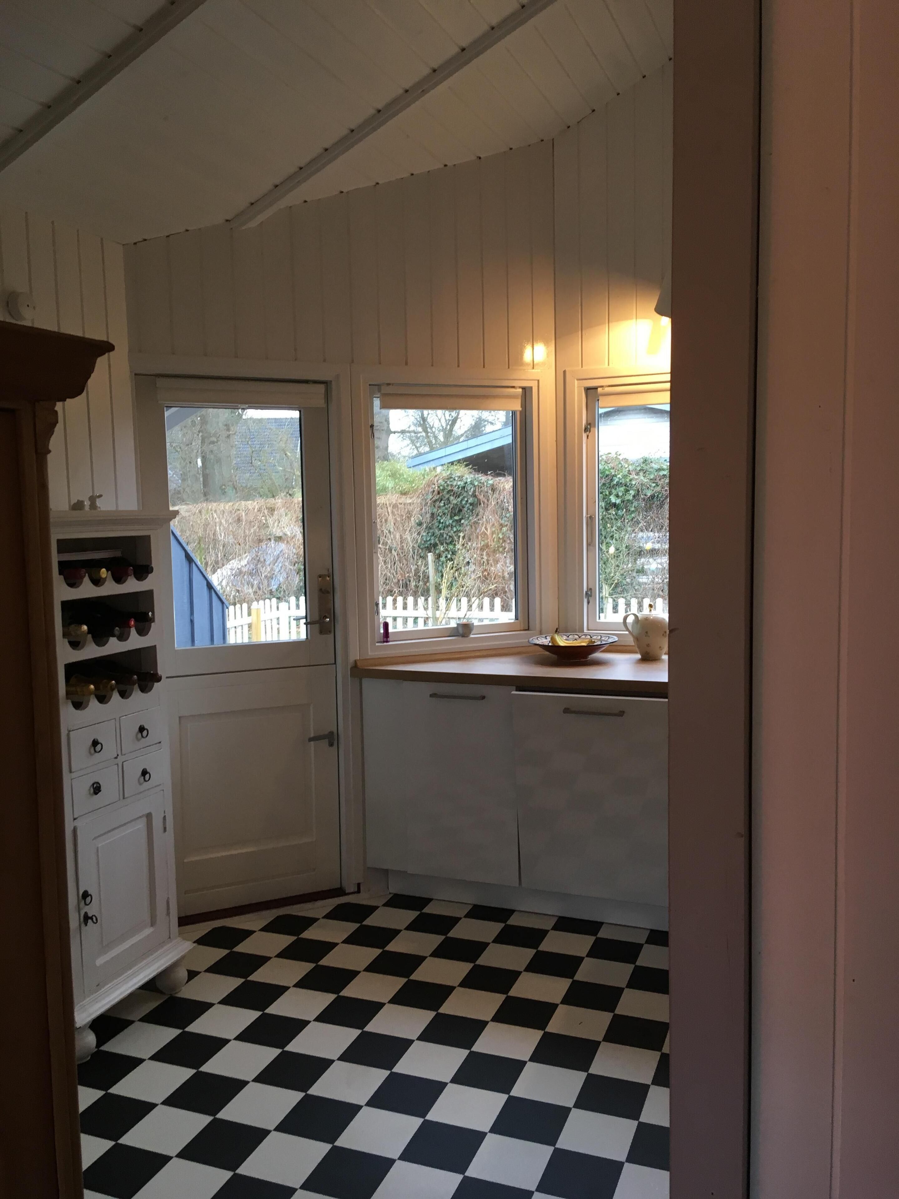 A kitchen with a checkered floor, white cabinets, and a window with a view of a fence and trees.