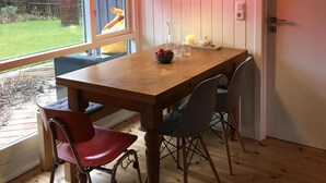 Un comedor con mesa de madera, dos sillas, una lámpara colgante roja y vista al exterior.