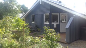 Una casa pequeña de azul oscuro con techo inclinado, un porche delantero y un jardín con diversas plantas y flores.