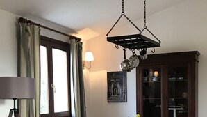 A dining area with a wooden table, six chairs, a hanging light fixture, a window with curtains, a wall-mounted lamp, and a cabinet with glass doors.