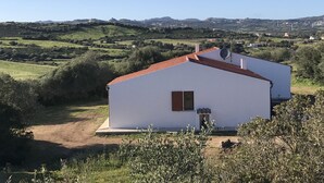 A white building with a red roof, surrounded by green fields and hills.